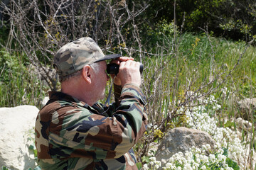 A man in camouflage clothing looks through a monocle in nature. Side view