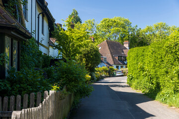 London, UK, 5 May 2025, A narrow road winding through a village with traditional houses and lush...