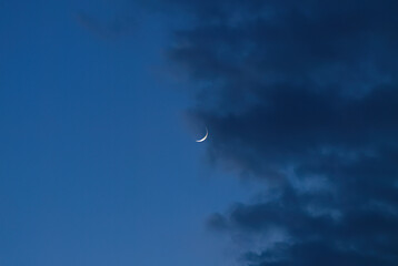 Crescent of the moon comes through the clouds, blue hour, blue sky and dark clouds, the crescent of the moon becomes visible, blue hour and moon © Rebecca