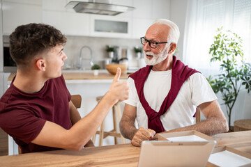 Young man gesturing thumbs up to his elderly father at home