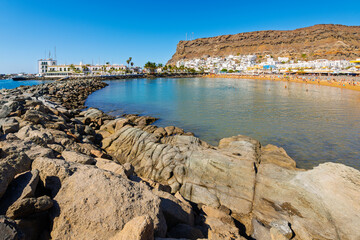 View from the Caleta de Mogan of the rocky breakwater, sandy Playa Mogan beach and whitewashed town of Puerto de Mogan, Spain, Las Palmas, Gran Canaria island.