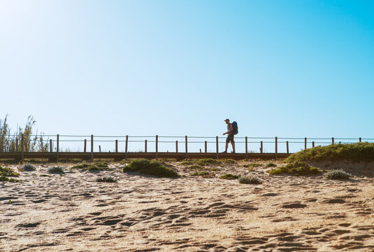 Lonely backpacker man walking by sandy Portugese beach in morning. Path leading by wooden passadicos  - boardwalks along the ocean coast. Shot during the Camino Portuguese —  popular pilgrimage route