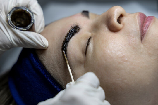 Henna eyebrow application: esthetician tinting client’s brows in beauty session