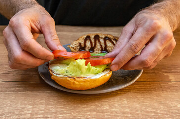 Chef hands preparing a hamburger with bread, salad and sausage. Delicious fast food burger prepared on a restaurant kitchen. Professional chef is preparing burger. Burger making.