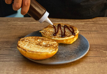 Chef hands spreading sausage in a bread to make a hamburger. Delicious fast food burger prepared on a restaurant kitchen. Professional chef is preparing burger. Burger making.