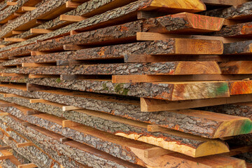 Piles of hardwood planks are arranged neatly at a lumber yard, showcasing natural textures, colors, and light reflecting off the surfaces