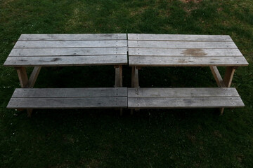 Top view of a weathered wooden picnic table with benches on a green grassy lawn in natural daylight