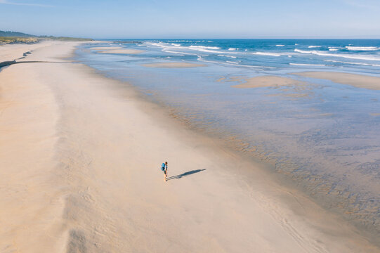 Aerial view of woman walking along sandy wide, long beach and enjoying Atlantic Ocean waves in Portugal. Shot during the Camino Portuguese —  popular pilgrimage route