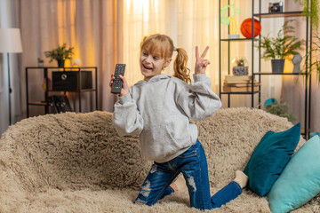 Young teenager girl increase volume at home tv, turning on cartoons with a remote and swaying...