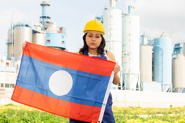 Sad young woman with helmet holding big flag of Laos against background of factory