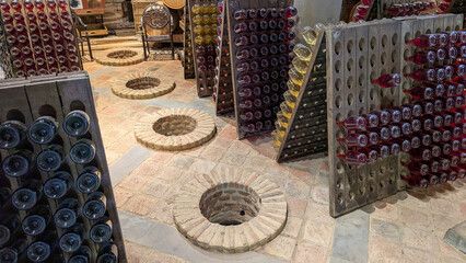 Wine bottles resting upside down on wooden riddling racks inside historic cellar, traditional brick...