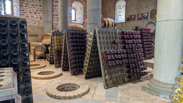 Vintage wine bottles positioned in wooden riddling racks near oak barrels, showcasing traditional sparkling wine production techniques in rustic winery cellar environment