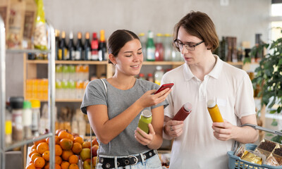 Couple young man and woman buyers scanning qr code for fresh smoothies in bottle in grocery store
