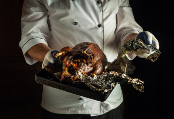 A chef proudly holds a tray displaying a beautifully roasted chicken wrapped in foil, revealing a...