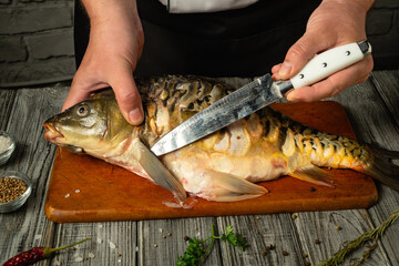 Hands expertly handling a fresh fish on a wooden board during the filleting process. The chef...