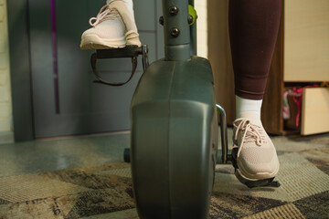 Individual exercising on a stationary bike indoors, wearing athletic shoes, showcasing a committed...