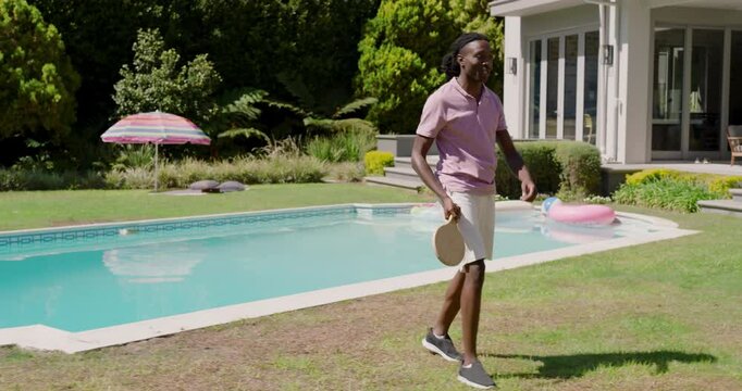 Diverse friends starting game by tossing yellow ball and volleying with paddles at backyard pool