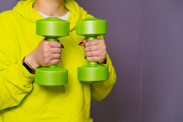 Woman in Yellow Hoodie Lifting dumbbell Against a Purple Wall