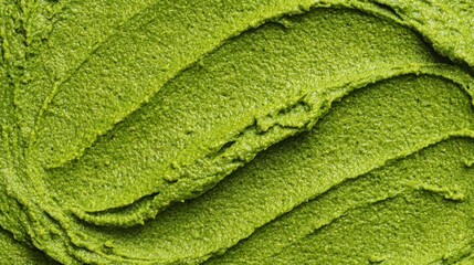 Bright green matcha powder is spread evenly across a flat surface, displaying a smooth and textured appearance under soft lighting, highlighting its vibrant color and fine consistency