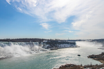 Stunning view of Niagara Falls with mist rising, surrounded by snow-covered banks and a bright blue sky above.