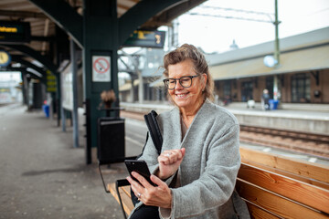 Happy senior woman at train station using smartphone