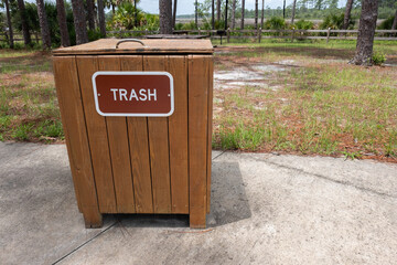 Clearly labeled trash can in a picnic are of a park