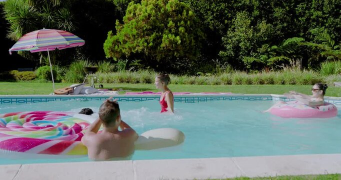 Diverse friends counting down leaping into backyard pool splashing donut float and swimming for fun