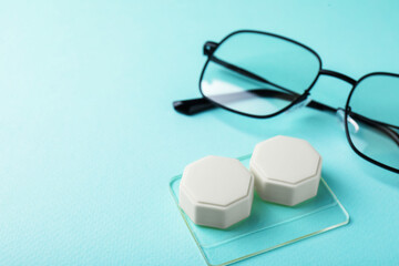 Contact lens case and glasses on turquoise background, closeup. Space for text