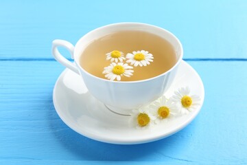Delicious chamomile tea in cup and fresh flowers on light blue wooden table, closeup