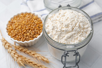 Wheat flour, grain and spikes on white tiled table, closeup