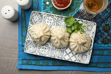 Delicious khinkali served with sauce and cilantro on grey table, flat lay