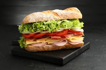 Tasty baguette sandwich with ham and vegetables on black table, closeup