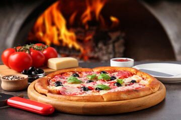 Freshly baked pizza and ingredients on grey table against oven