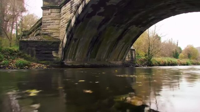 Autumnal river scene underneath old stone bridge tranquil river and bridge picturesque landscape underneath bridge river scenery background image outdoor autumn river