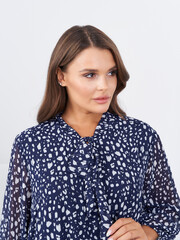 Woman with long brown hair wearing a patterned navy blouse looks to the side. Small, white spots...