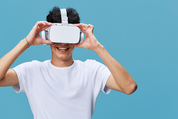 Naklejka premium Young man wearing virtual reality headset enjoying immersive digital experience, smiling and relaxed against blue background in casual white t-shirt.