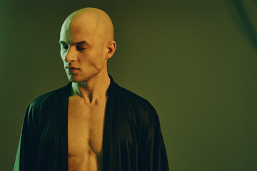 A contemplative man in a dark robe, showcasing a serene expression and bald head. The soft green...