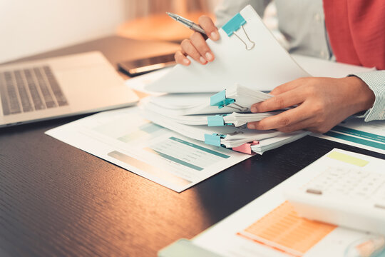 Professional woman checking charts and financial data with calculator and laptop and analyzing and reviewing. Close-up of young woman working with paper documents on desk.