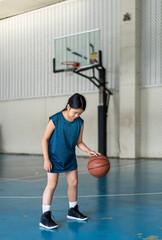 basketball by asian child or kid girl playing training to learning bouncing and left hand raising ball or young children at sports stadium school or gymnasium basketball court for sport day exercises
