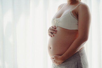 Young happy pregnant woman posing in studio with white curtains in background
