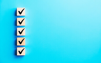 Checklist Icon on Blue Background: Five wooden blocks with check marks aligned on the left against a vibrant blue background. This minimalist graphic suggests completion, planning, and order. 