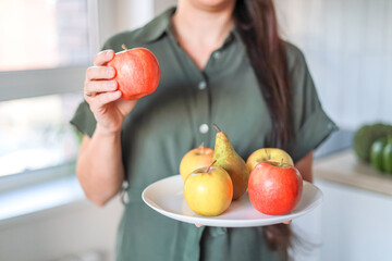 Close-up Fresh apples and pears on a white plate in the hands of a woman in the kitchen. Dietetics, healthy eating, vegetarianism, veganism, raw food, recipe, menu