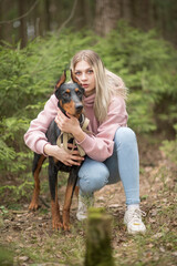 Portrait of young beautiful blonde girl with Doberman outdoors.