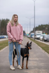 Portrait of young beautiful blonde girl with Doberman outdoors.