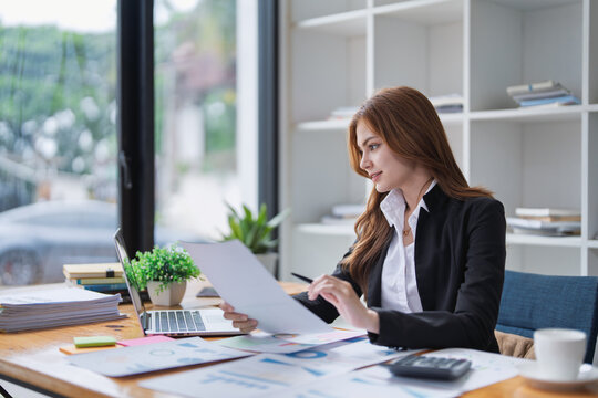 Elegant businesswoman analyzes financial reports at her office desk inside.