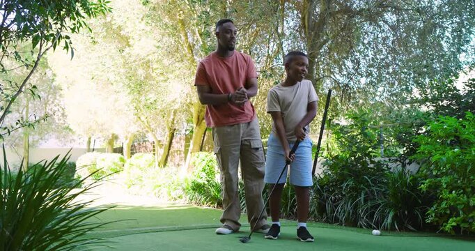 African American father and son at backyard green guiding putter grip, ball dropping, teaching golf