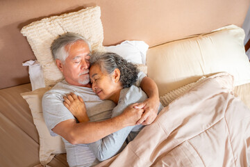 Happy Asian family senior couple sleeping on bed and holding hands together. Elderly retired husband and wife comfort relaxing, taking care each other. Old people healthcare and family relationship.