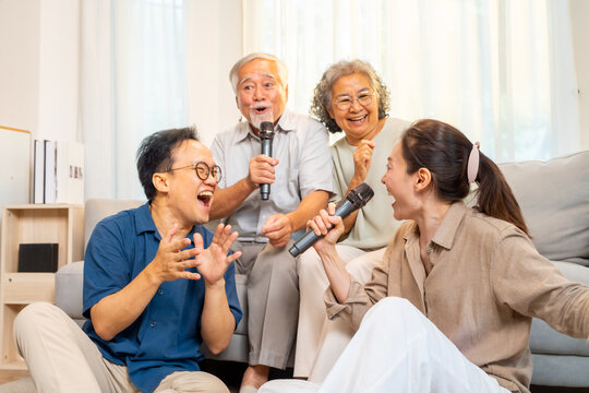 Happy Asian family senior parents and adult child spending time together at home. Healthy elderly father and mother enjoy and fun singing karaoke song dancing with daughter and son in living room.