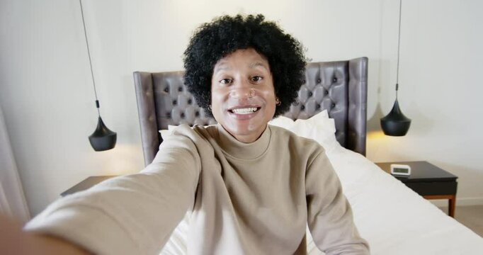 Mid adult African American man adjusting camera flashing peace-sign pointing on bed in bedroom