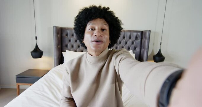 African American man leaning forward adjusting camera brushing hair, speaking on bed for vlogging